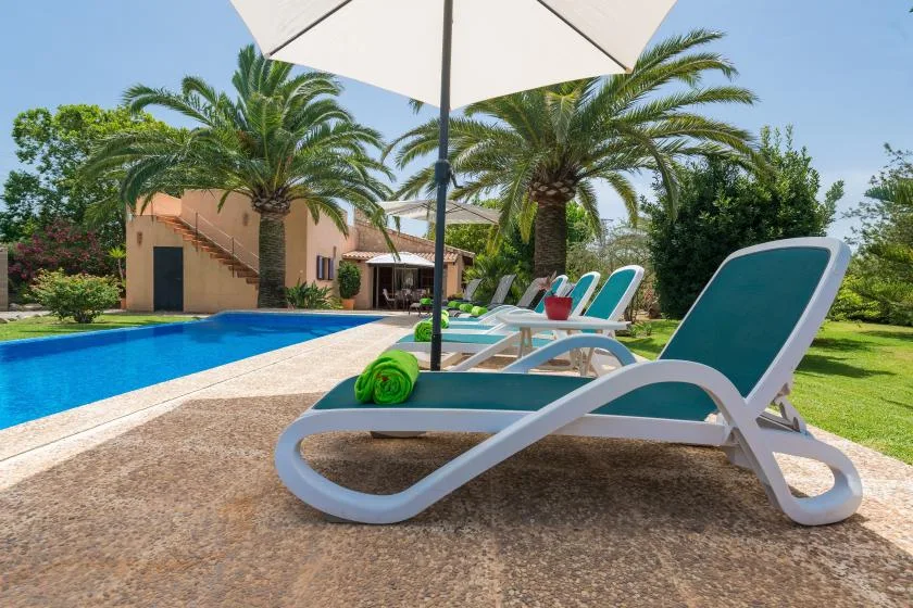 An outdoor poolside scene with reclining loungers beneath a large umbrella.