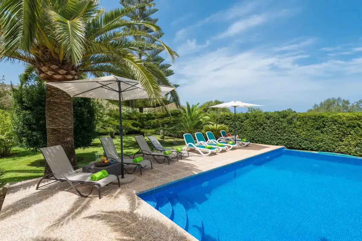 An outdoor swimming pool is surrounded by lounge seating and greenery.
