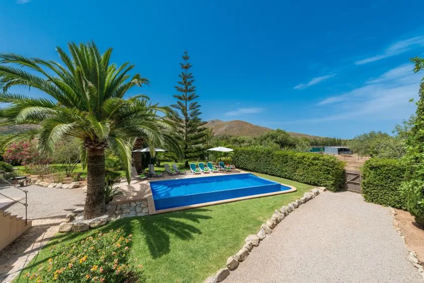 An outdoor swimming pool is surrounded by greenery and paved paths.