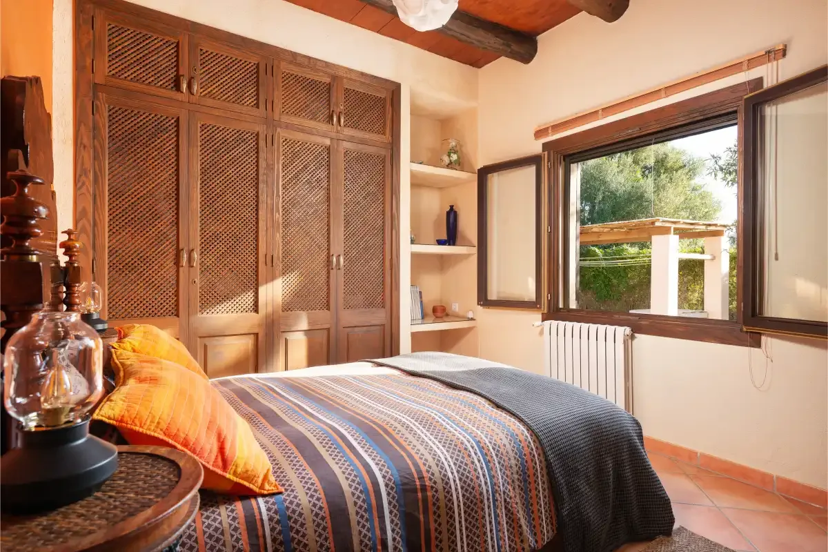 A bedroom with a patterned bedspread and a large window overlooking greenery.
