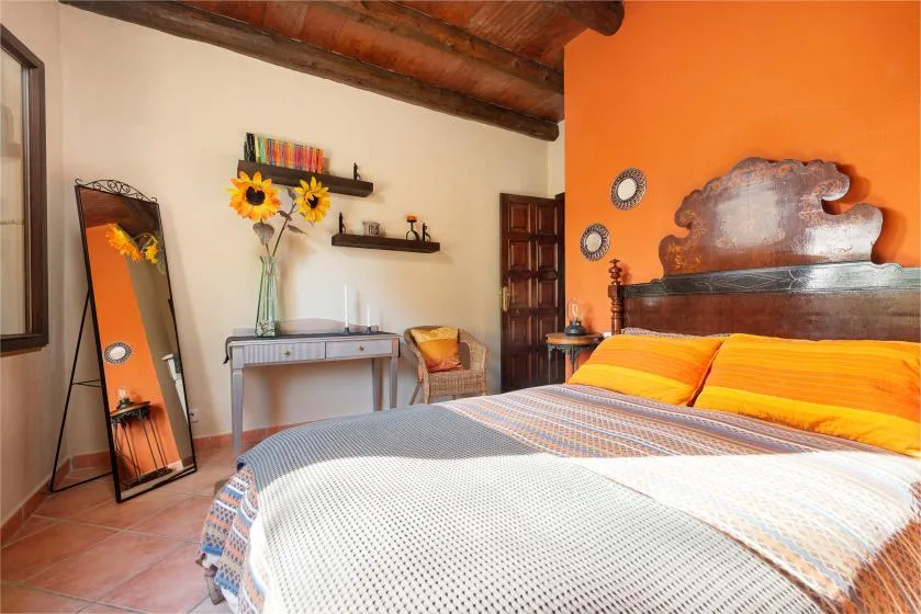 A bedroom with a large bed, orange accent wall, and a small dressing table.