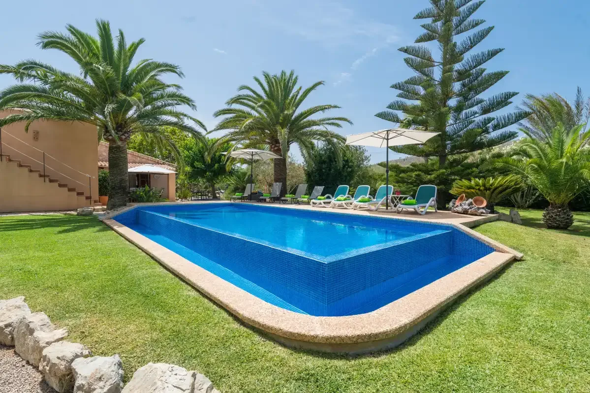An outdoor swimming pool is surrounded by lawn, palm trees, and lounge seating.