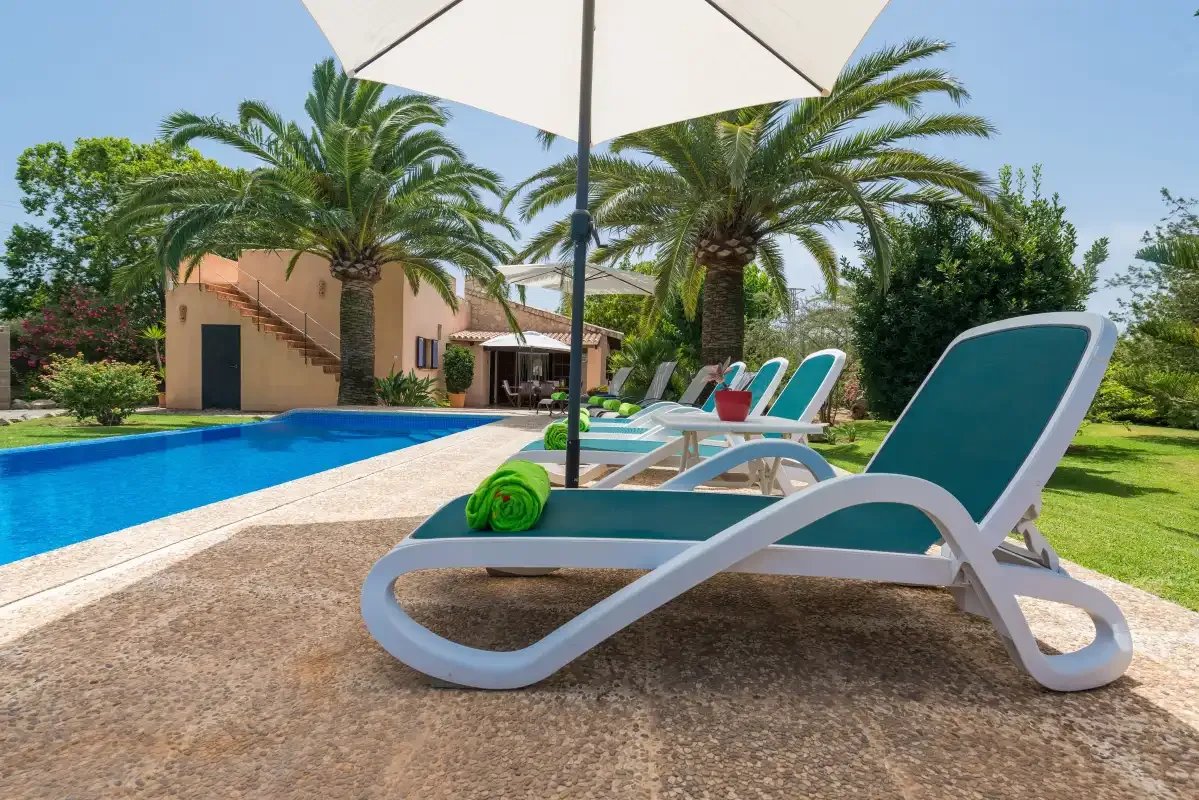 An outdoor swimming pool beside reclining seating and palm trees.