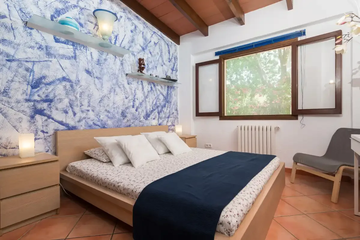 A bedroom with a bed, patterned accent wall, and a large window.