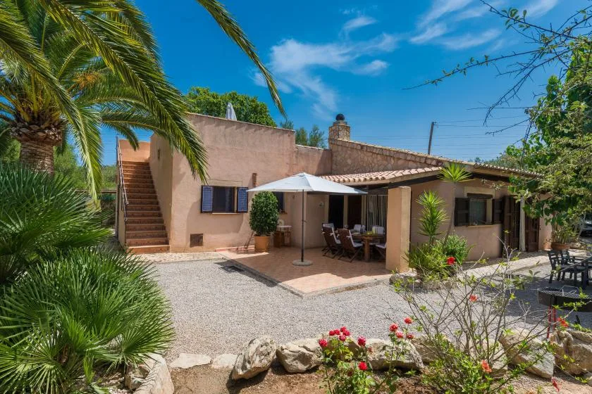 A low house opens onto a gravel courtyard with shaded outdoor seating.