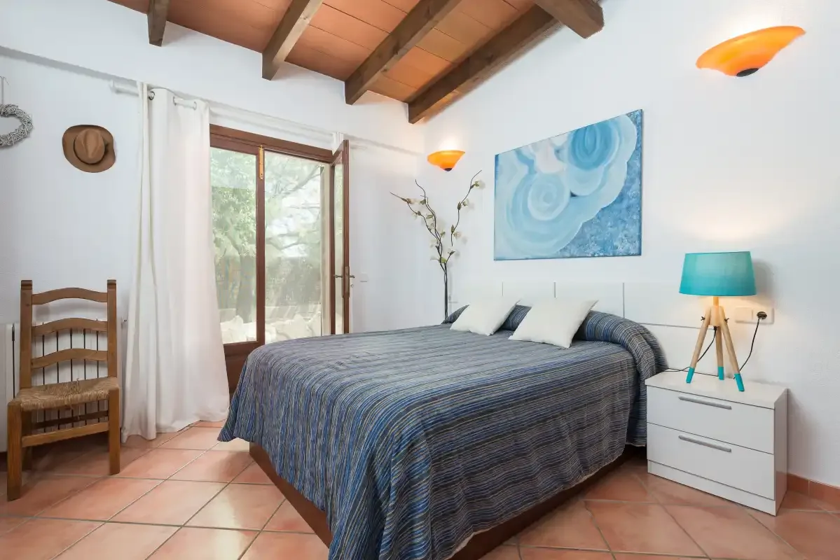A bedroom with a bed, a wooden chair, and a window.