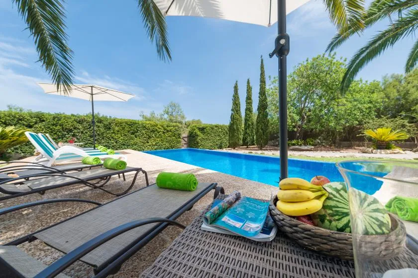 A sunny poolside patio with lounge seating and a fruit basket.
