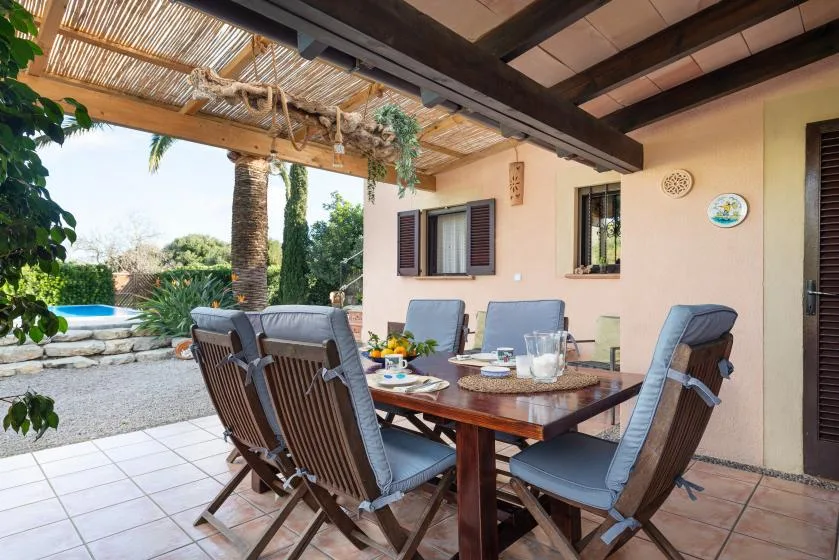 A covered patio dining area with a table and cushioned seating.