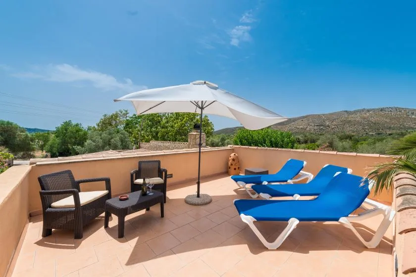 A sunny terrace has blue lounge chairs, a table, and a large white umbrella.