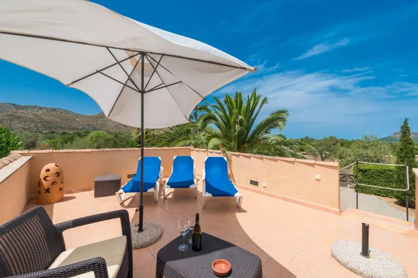 A sunny outdoor terrace has blue lounge seating beneath a large umbrella.