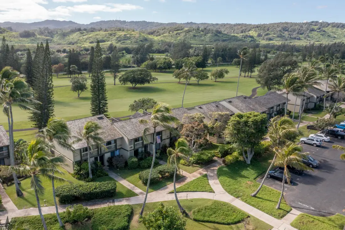 Aerial view of low-rise buildings and landscaped grounds beside a broad green field.