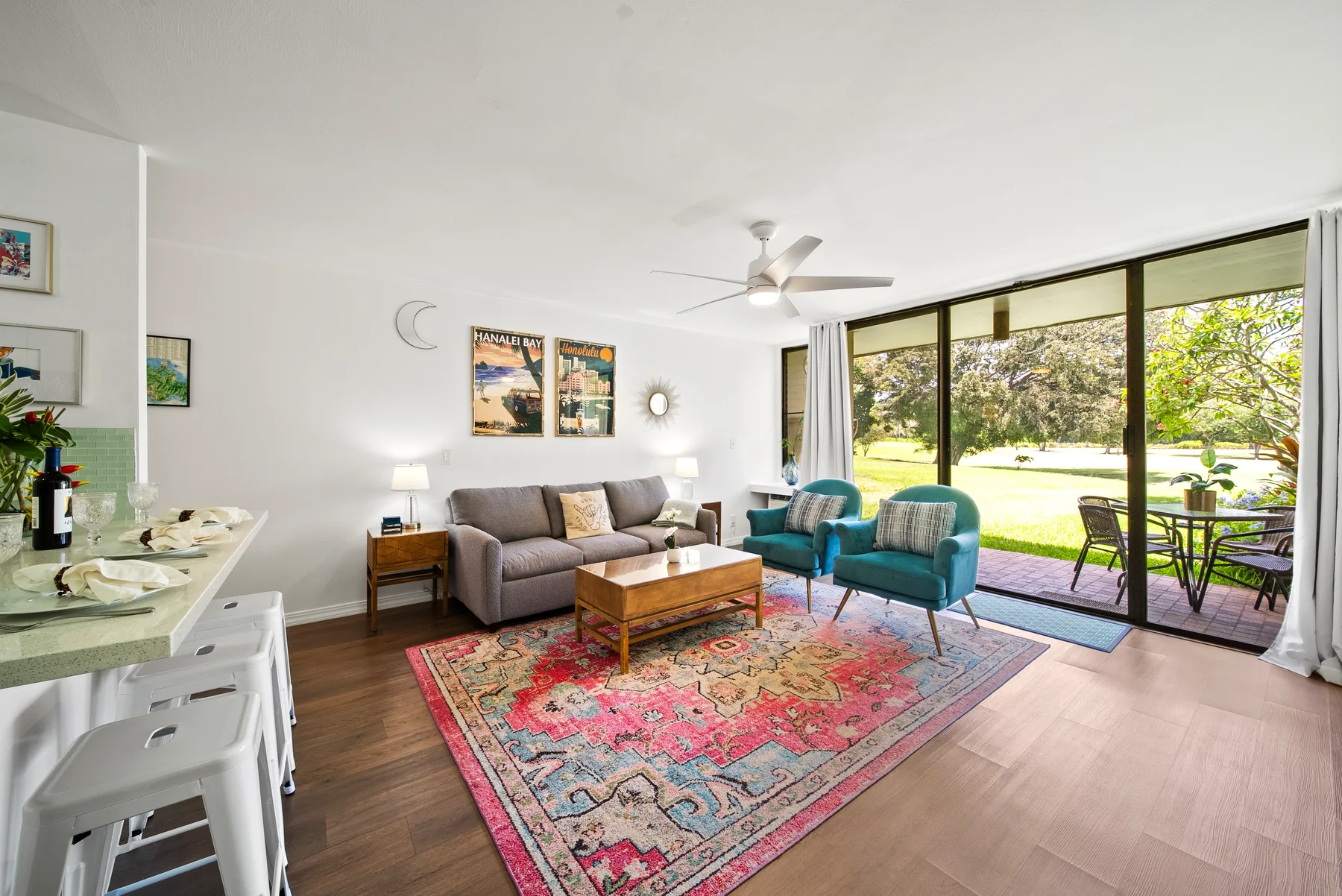 A bright living room with seating around a colorful patterned rug beside large windows.