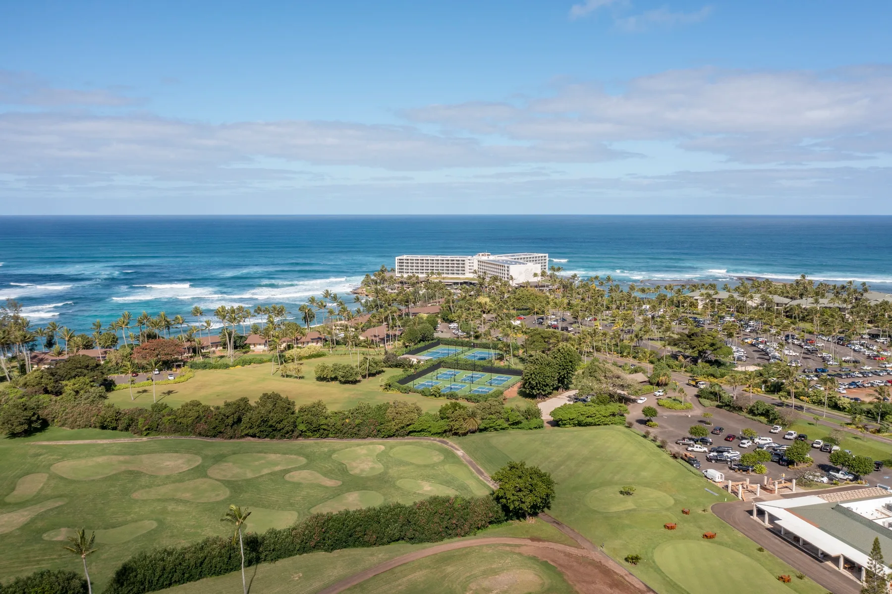 A coastal resort landscape with ocean waves, greenery, and tennis courts.