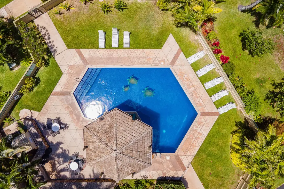An aerial view shows a blue swimming pool surrounded by paving and lawn.