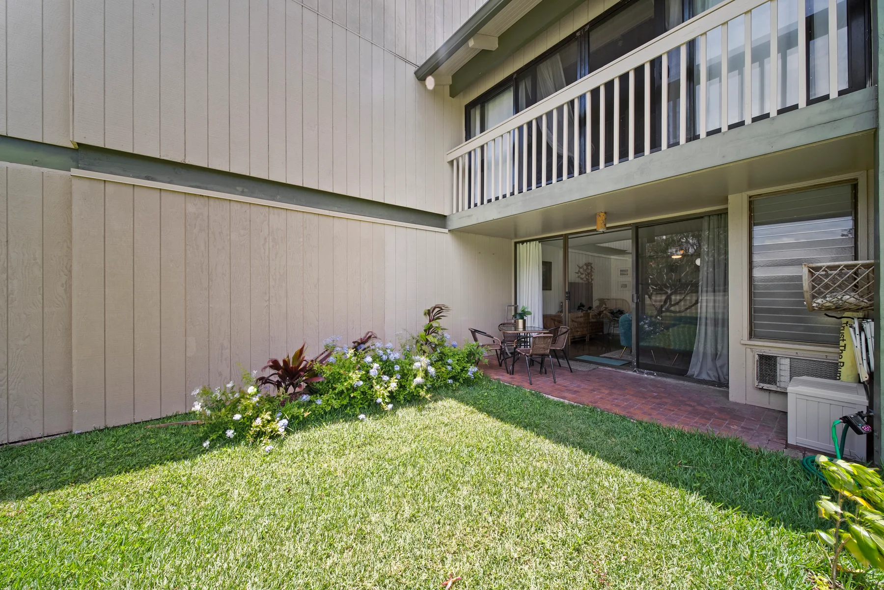 A grassy courtyard garden sits beside a two-story building with a patio.