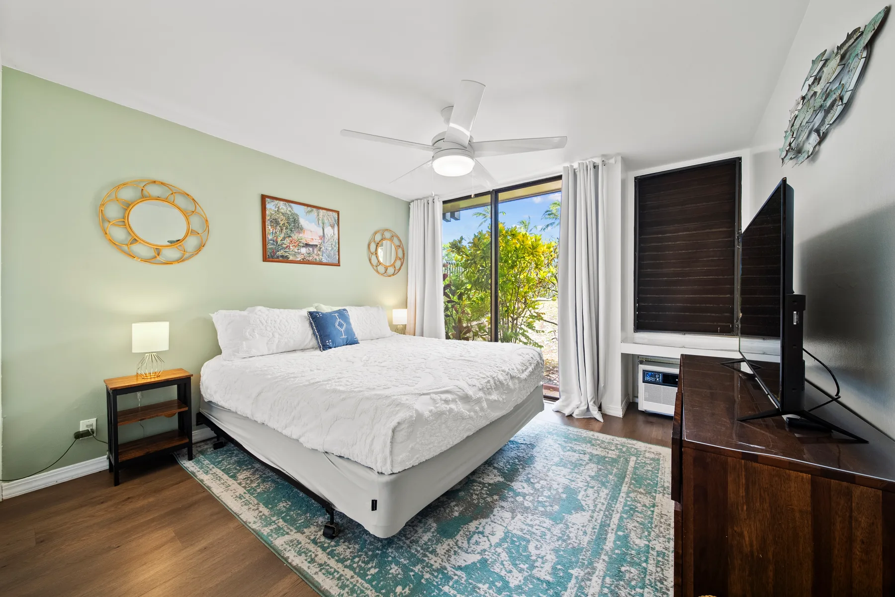 A bedroom with a bed, ceiling fan, and sliding glass doors opening to greenery.