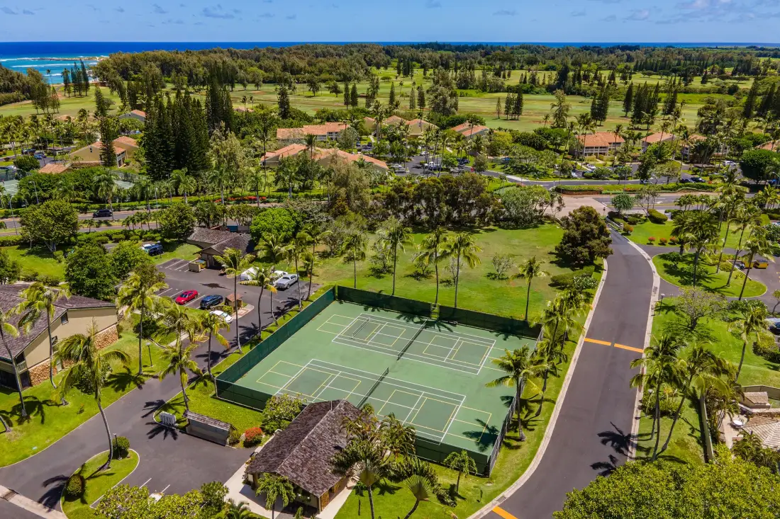 An aerial view shows tennis courts beside a landscaped resort grounds.