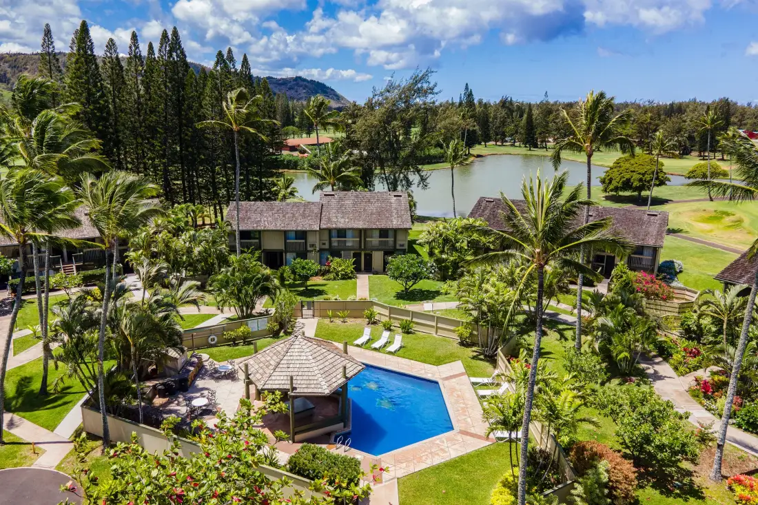 A landscaped resort grounds with a swimming pool, garden paths, and a lake.