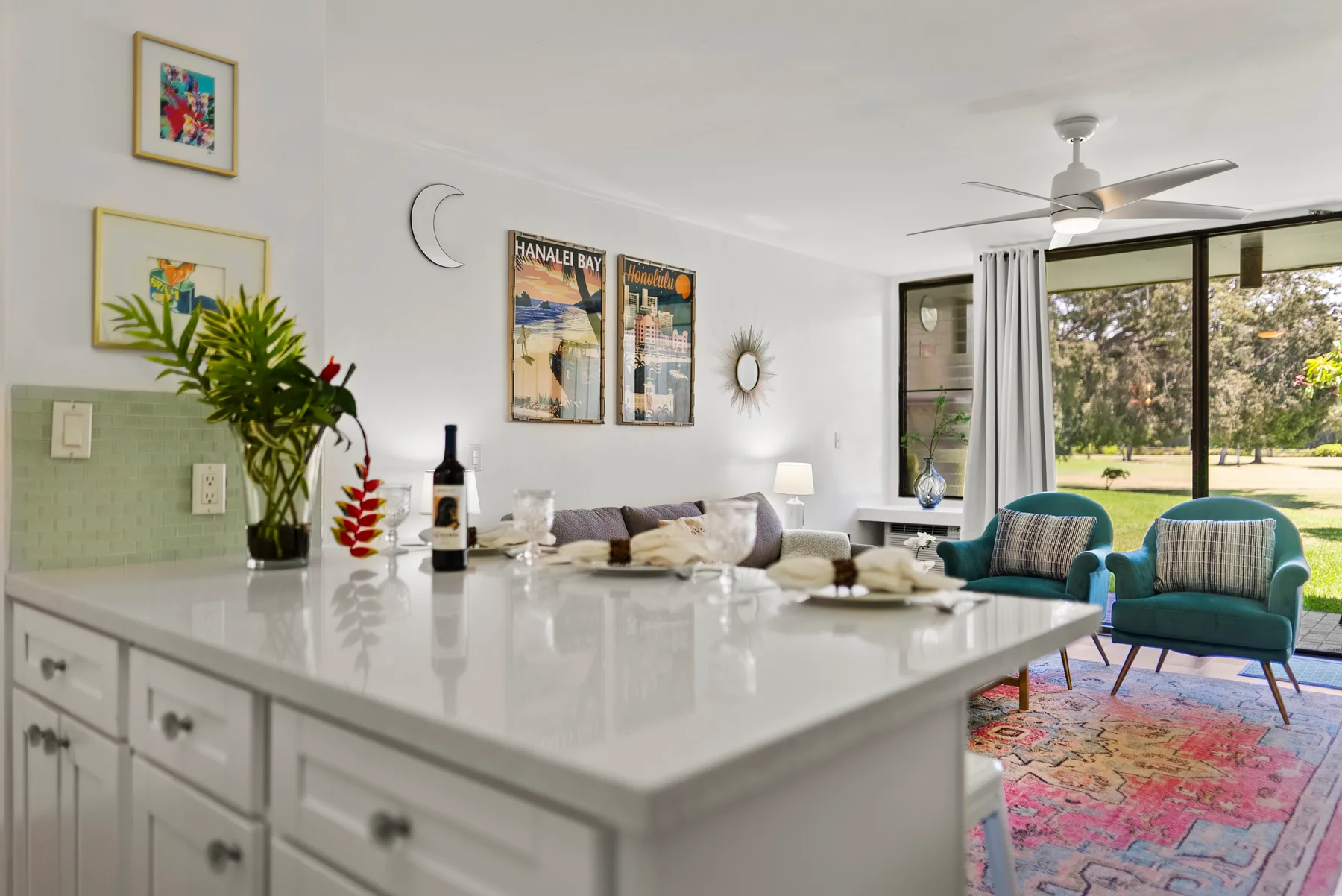 A bright living room with teal seating beside a large window overlooking greenery.
