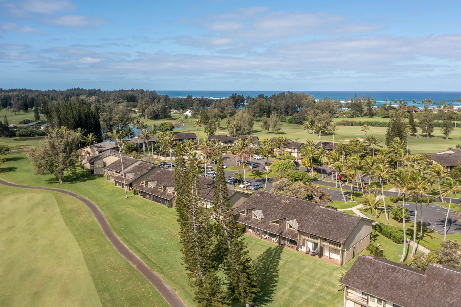 Aerial view of low-rise buildings amid green grounds, with the ocean in the distance.