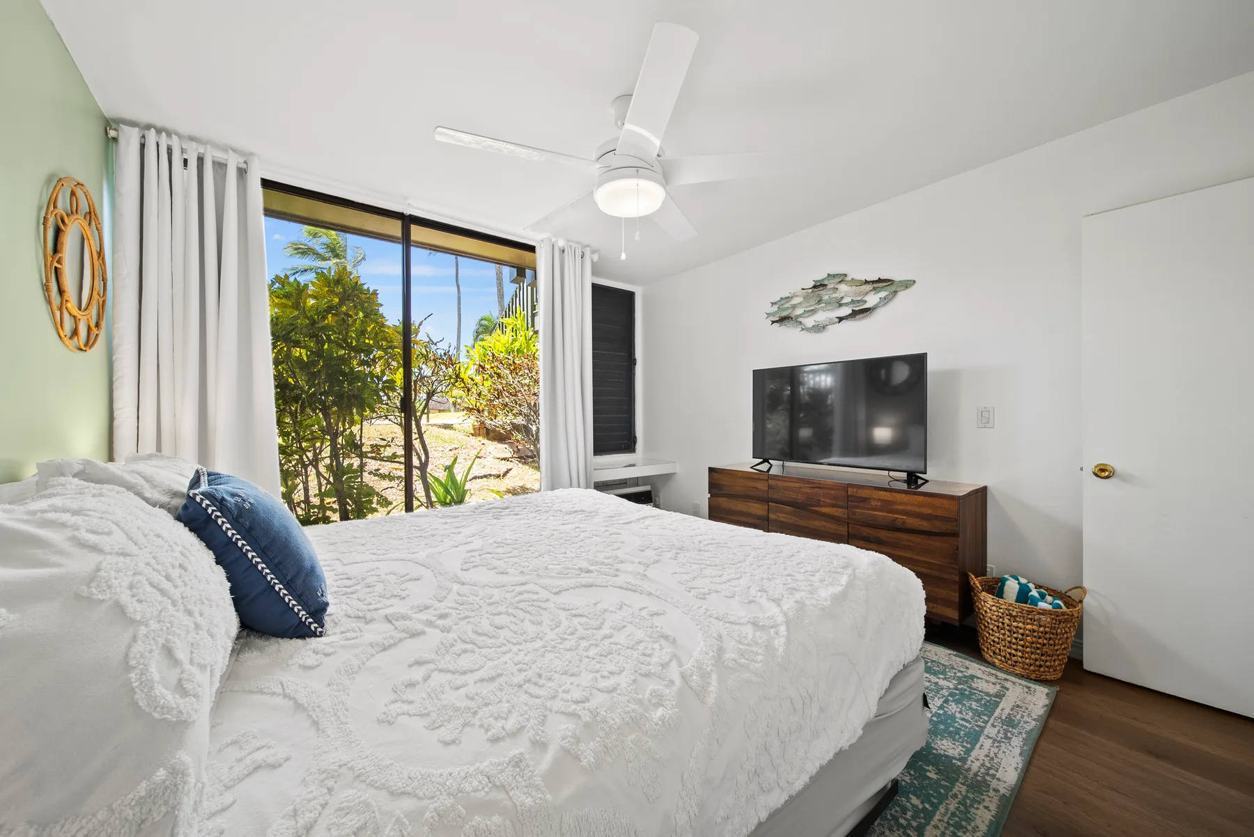 A bright bedroom with white bedding, a television, and sliding glass doors opening to greenery.