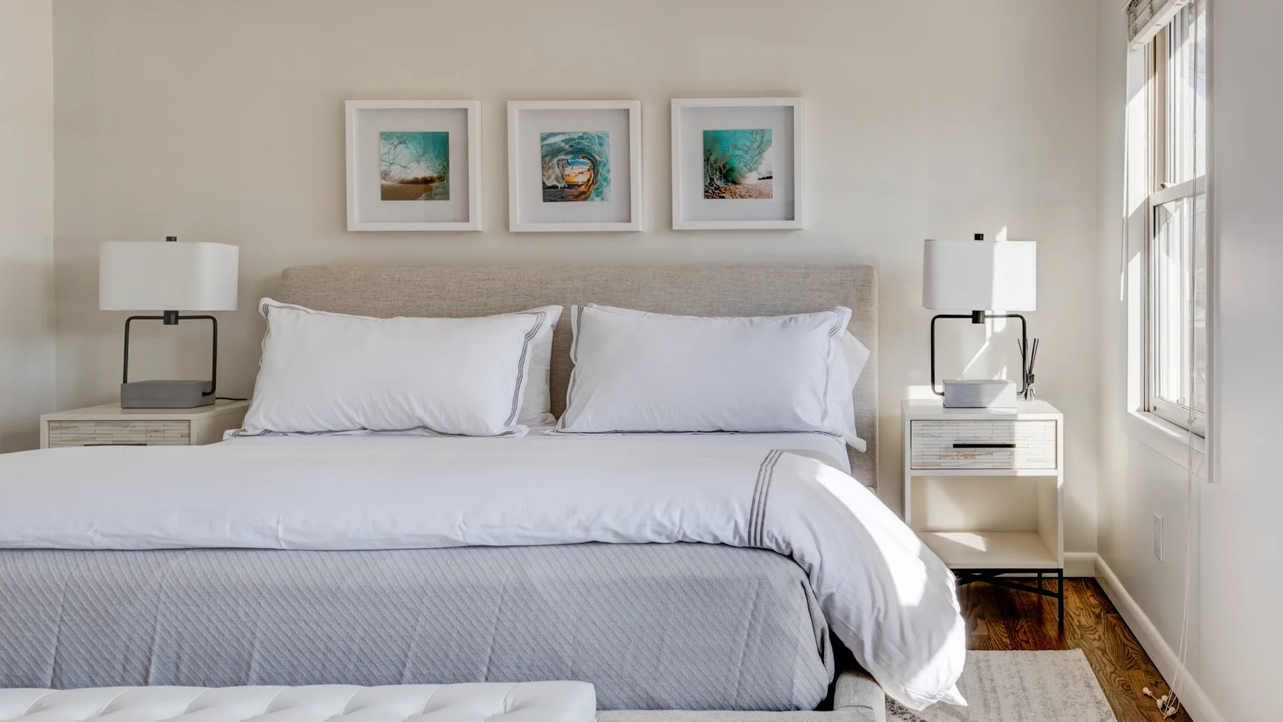 Un dormitorio luminoso con una cama bien tendida y cuadros sobre el cabecero.