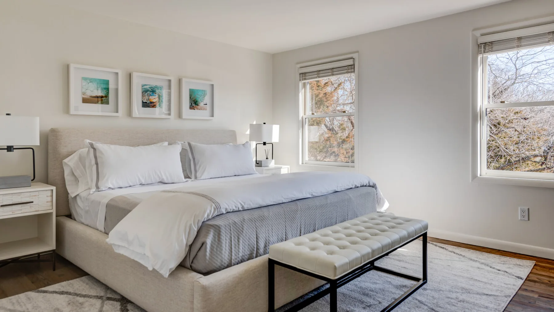 Un dormitorio luminoso con una cama tendida y un banco acolchado a sus pies.