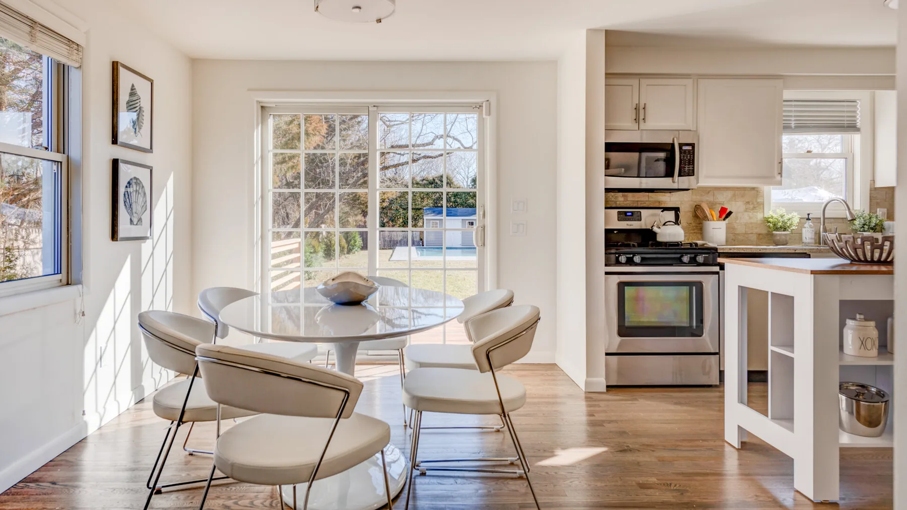Un comedor luminoso con una mesa redonda junto a una cocina y grandes ventanas.