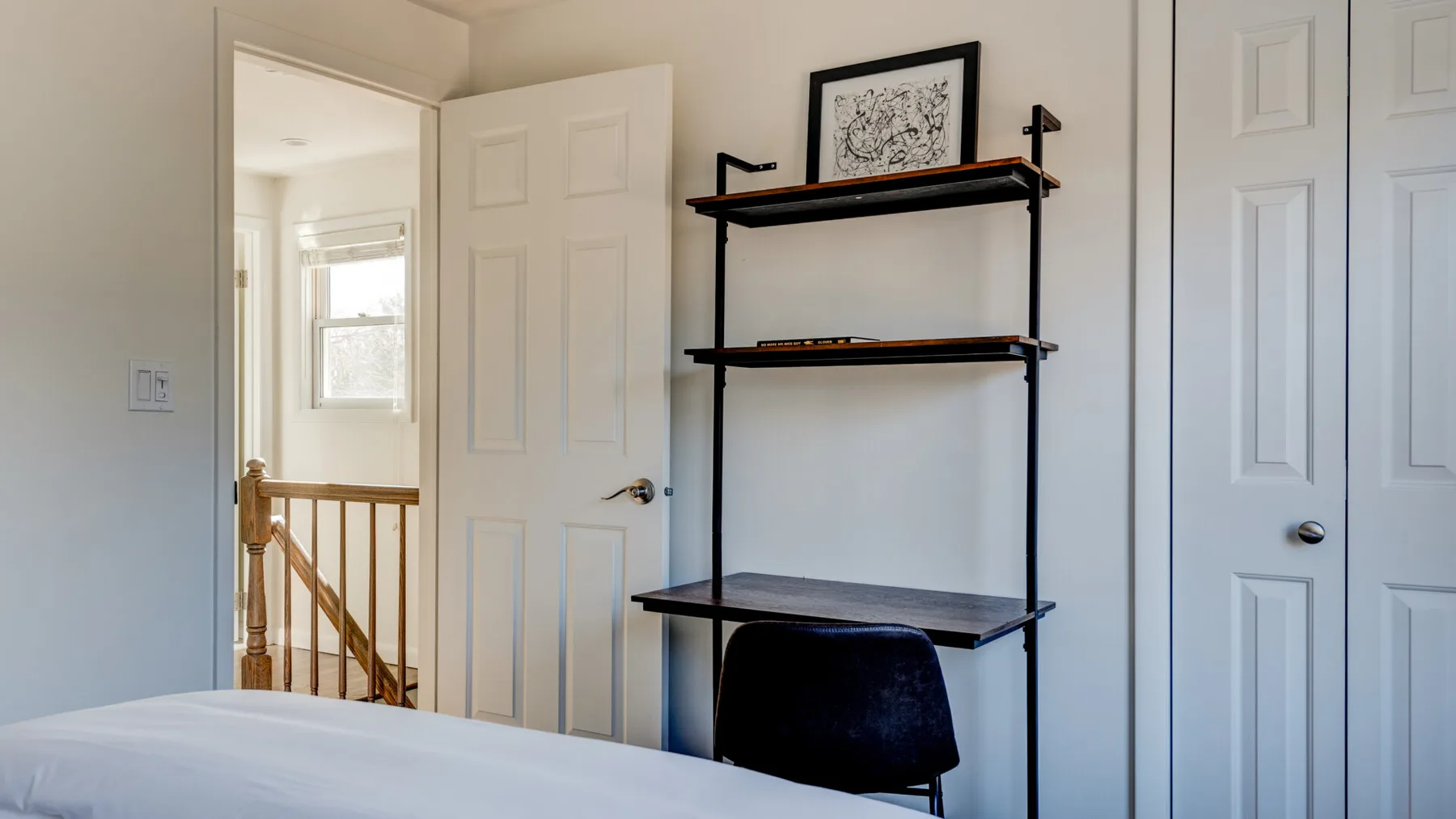 Un dormitorio con un escritorio oscuro y estantes junto a una puerta abierta.