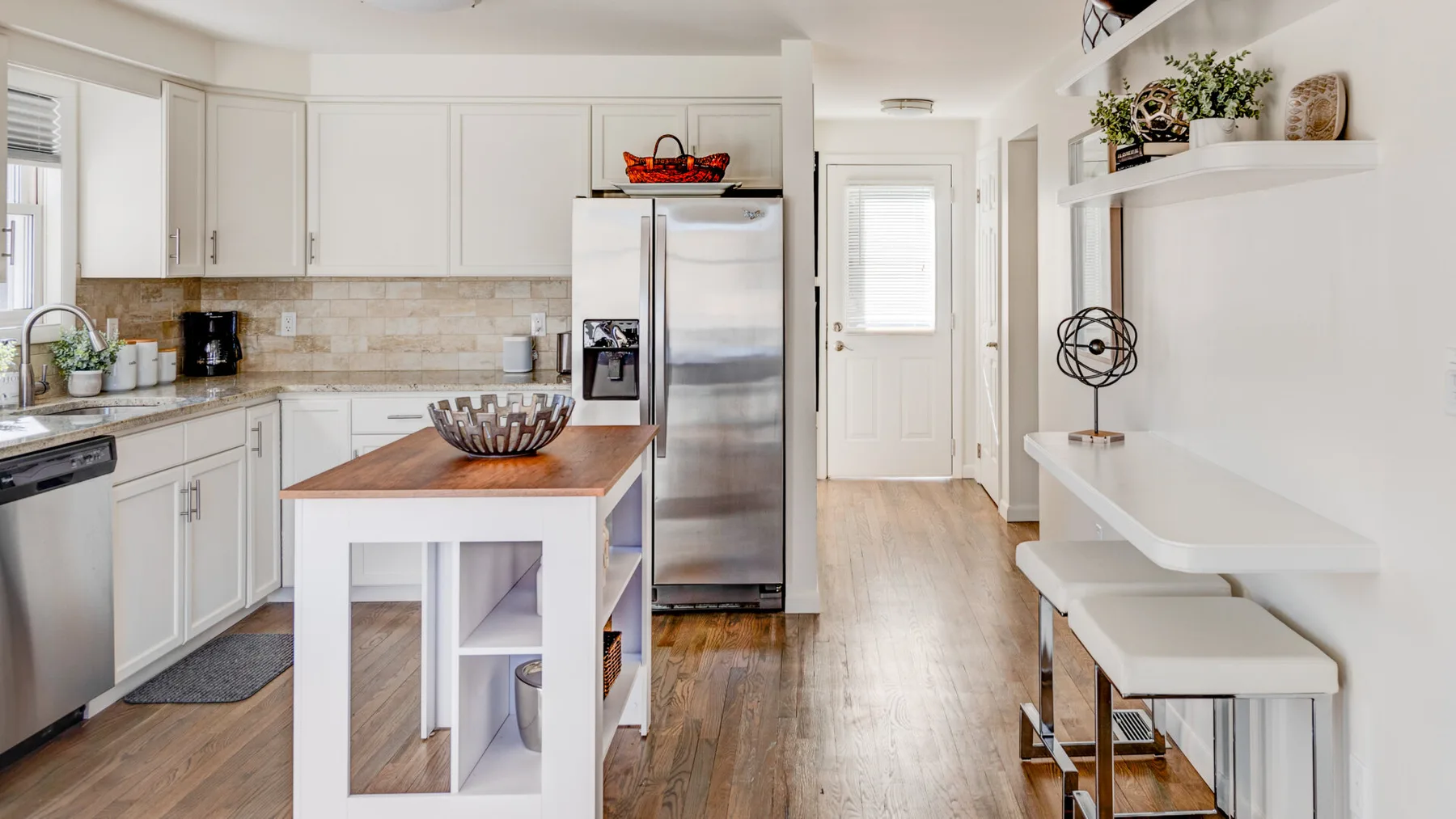 Una cocina luminosa con gabinetes blancos, electrodomésticos de acero inoxidable y una isla central.