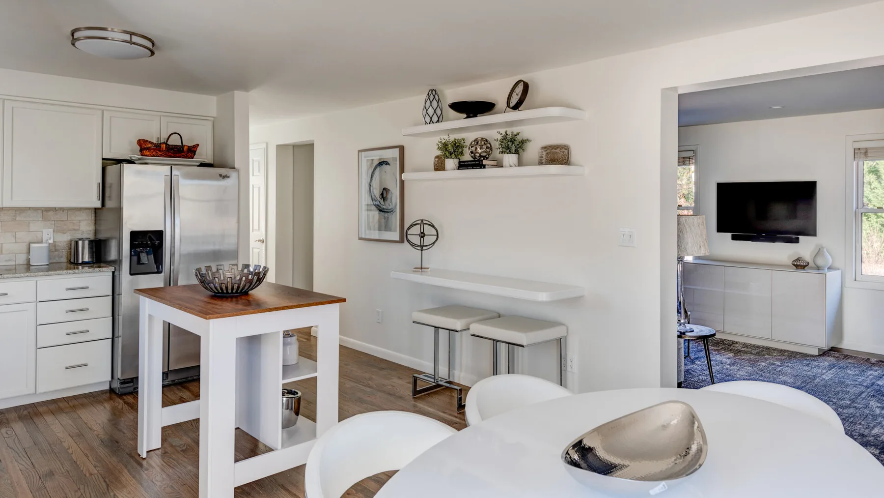 Una cocina luminosa con una isla pequeña y una sala de estar contigua.