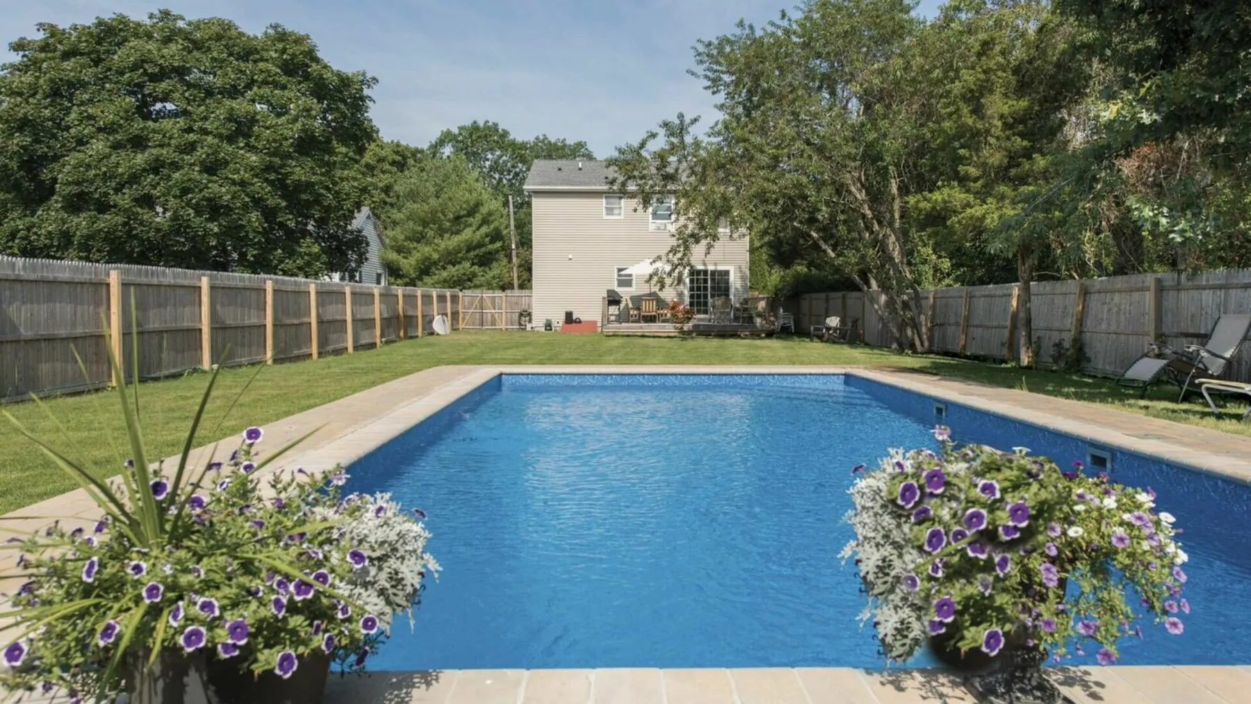 Una piscina en el patio está rodeada de jardineras con flores y una cerca de madera.