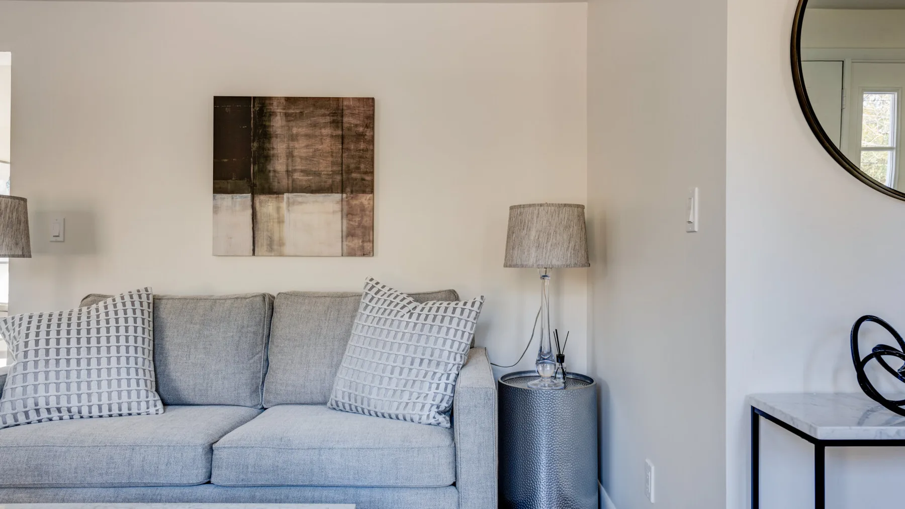 Una sala de estar con un sofá gris, cojines estampados y arte mural.