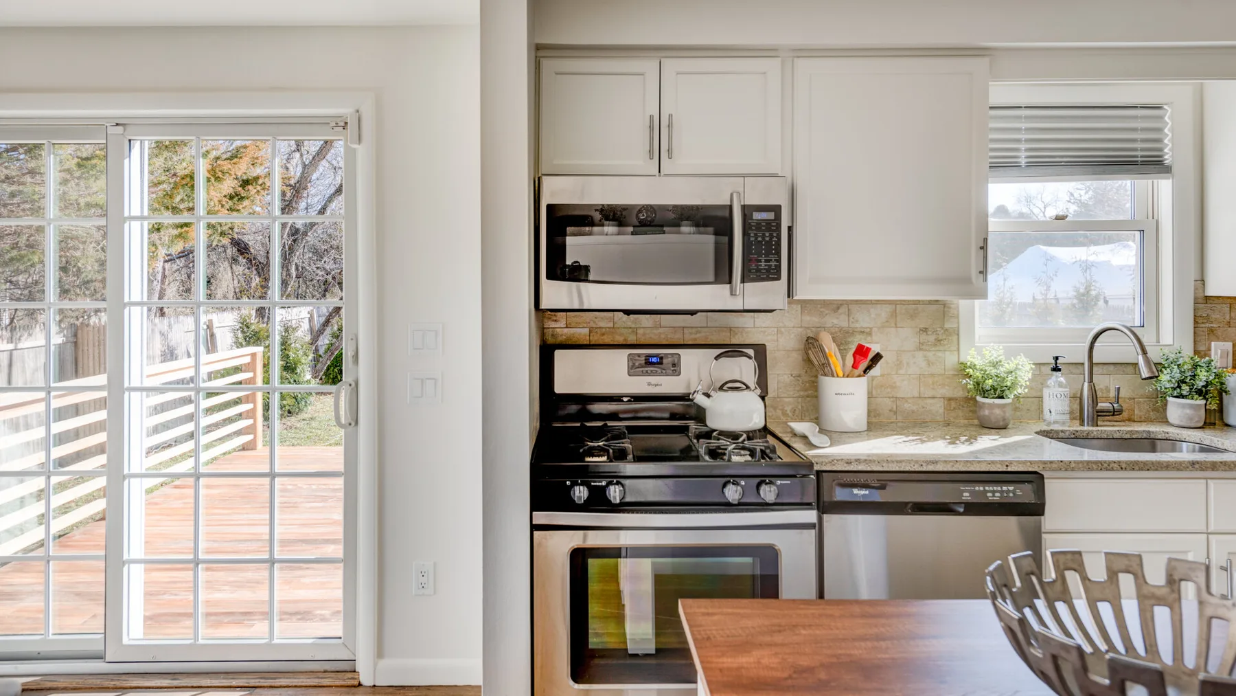 Una cocina luminosa con gabinetes blancos, una estufa de gas y una mesa de madera.