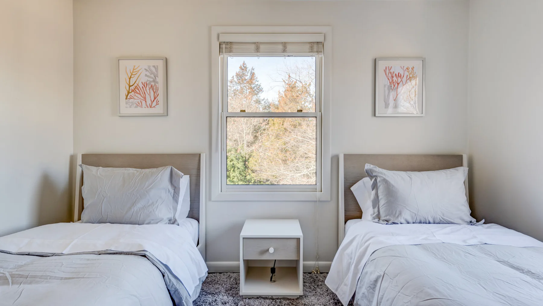 Un dormitorio luminoso con dos camas y una ventana entre ellas.