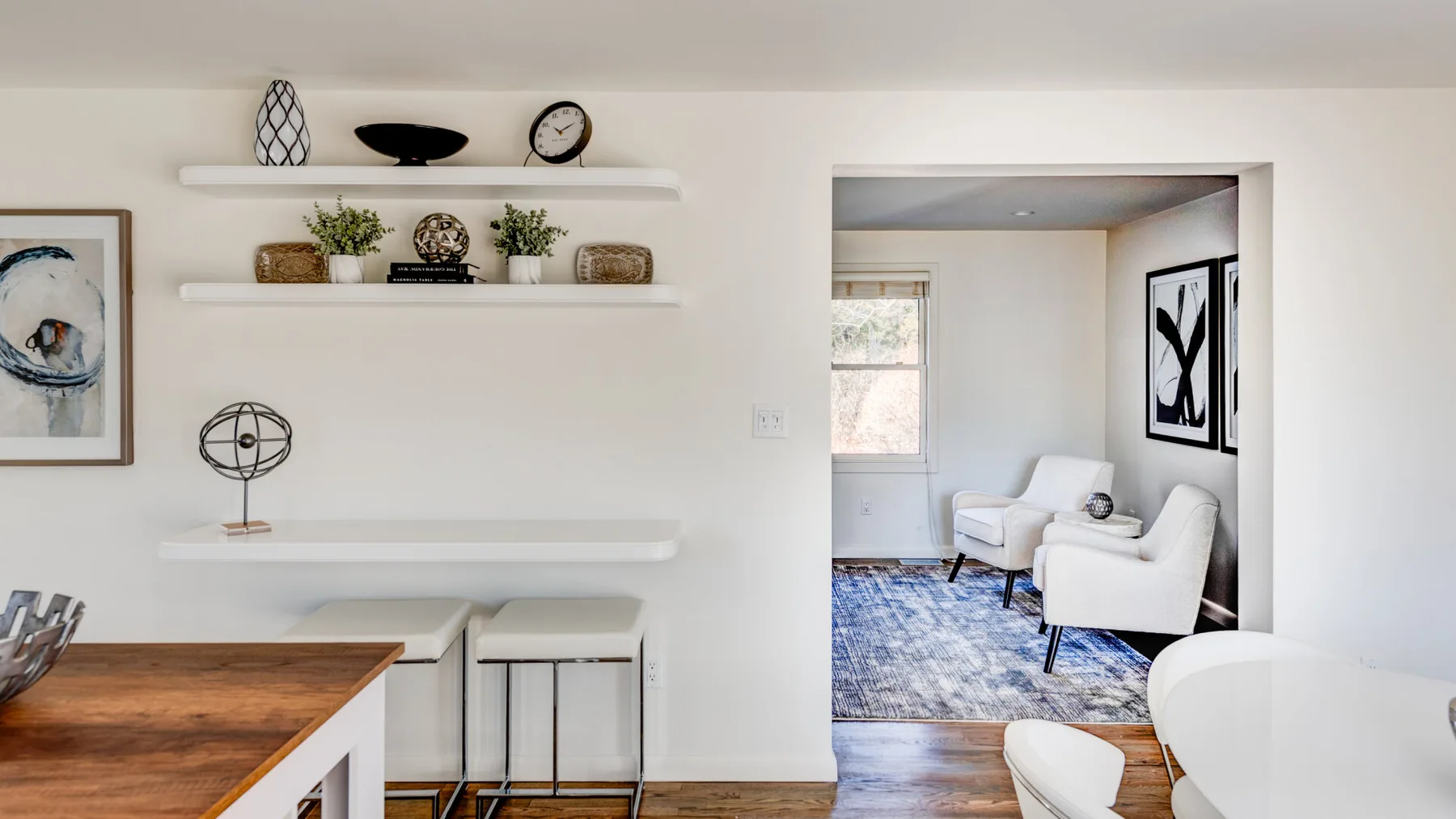 Una sala luminosa con asientos blancos, estantes de pared y obras enmarcadas.