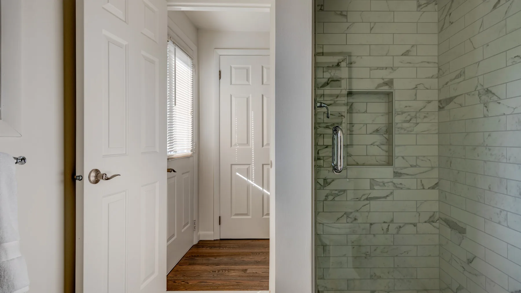 Un baño con una ducha alicatada y una puerta hacia una habitación con suelo de madera.