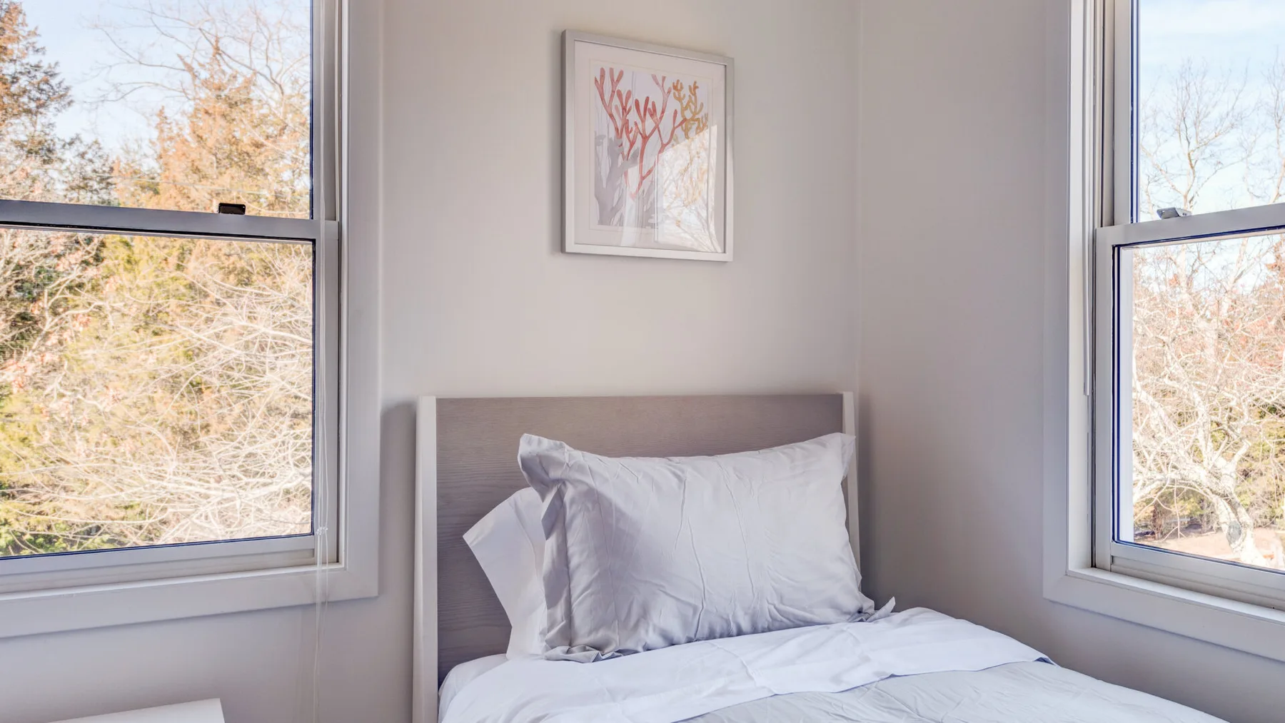 Un dormitorio con una cama entre dos ventanas y un cuadro en la pared.