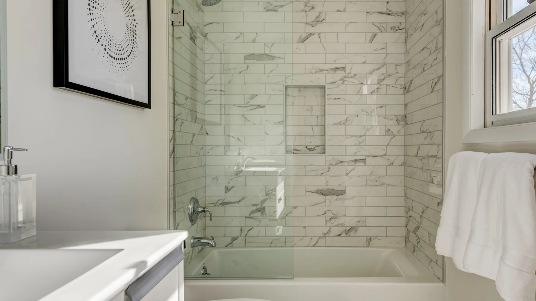 Una ducha de baño con azulejos junto a un lavabo y una ventana.