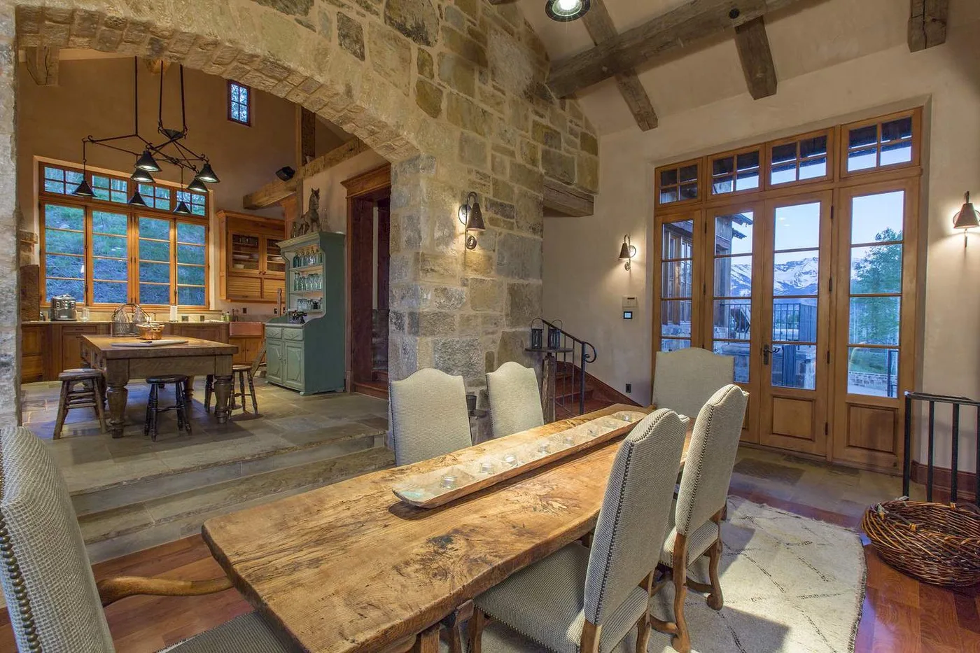Un comedor con una mesa de madera junto a grandes ventanas y un arco de piedra.