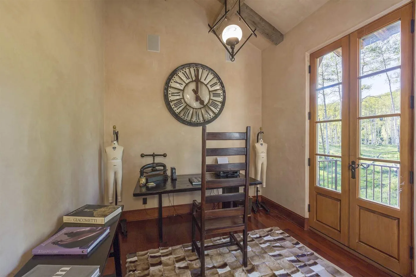 Un pequeño espacio de estar con mesa de madera, reloj de pared y puertas acristaladas.
