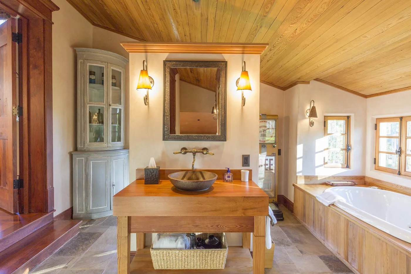 Un baño luminoso cuenta con un tocador de madera, un espejo grande y una bañera.