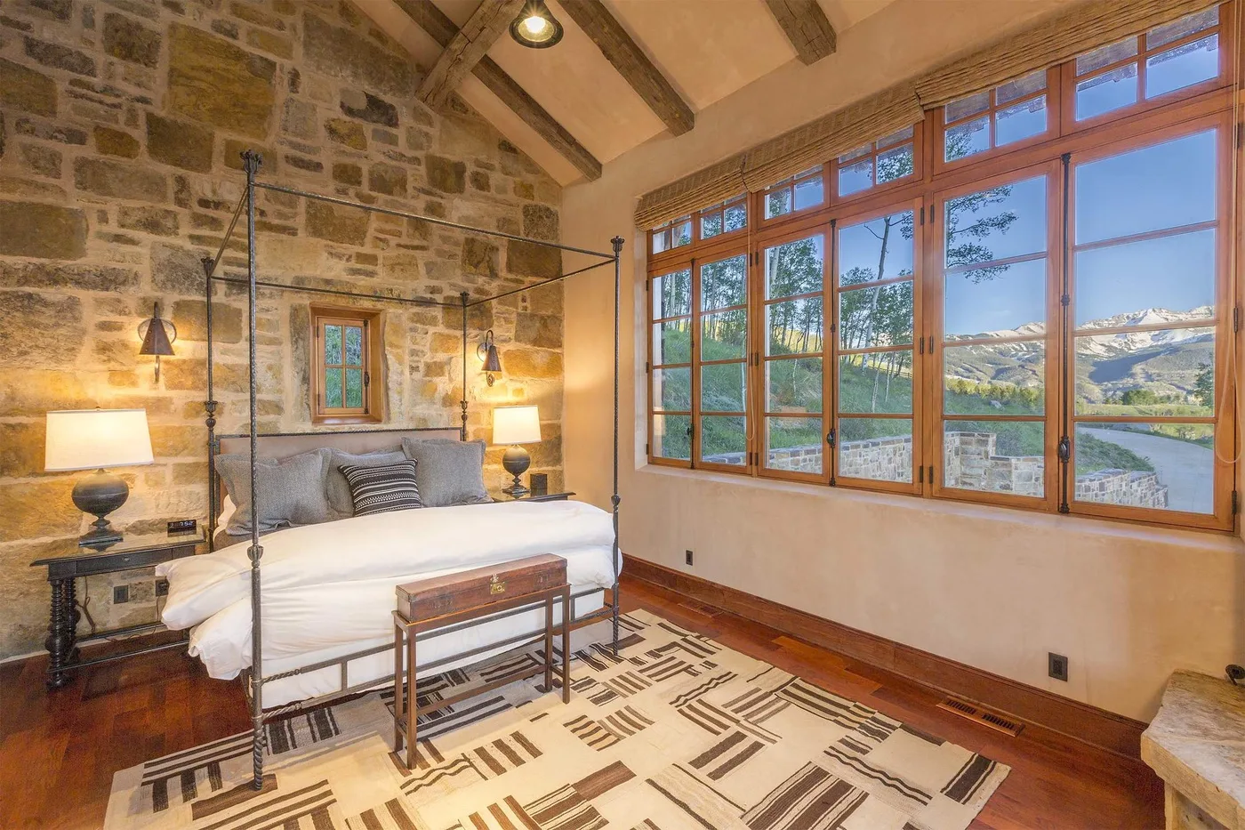 Un dormitorio con una cama bajo vigas expuestas y grandes ventanas con vistas al paisaje.