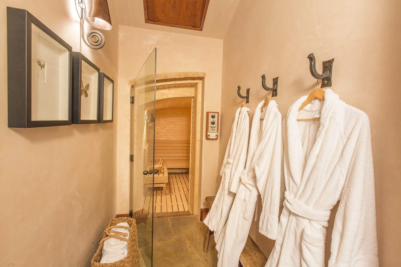 Una zona para cambiarse en el baño, con batas blancas junto a la puerta abierta de una sauna.