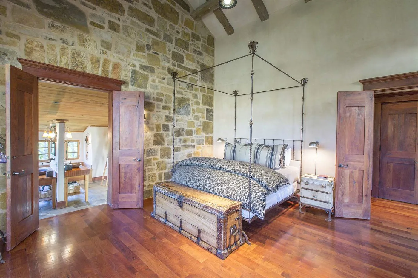 Un dormitorio con una cama con dosel, una pared de piedra y suelo de madera pulida.