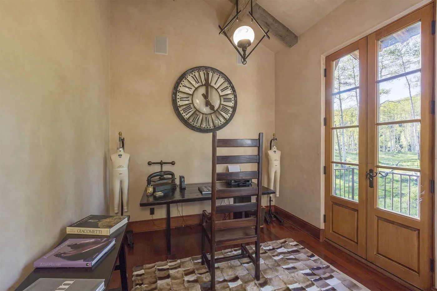 Una pequeña zona de escritura con escritorio, silla y reloj grande junto a puertas acristaladas.