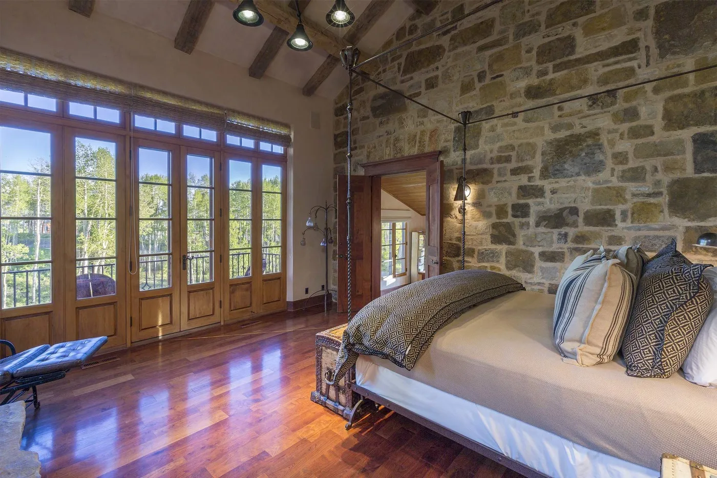 Un dormitorio con una cama grande junto a ventanas altas y paredes de piedra a la vista.