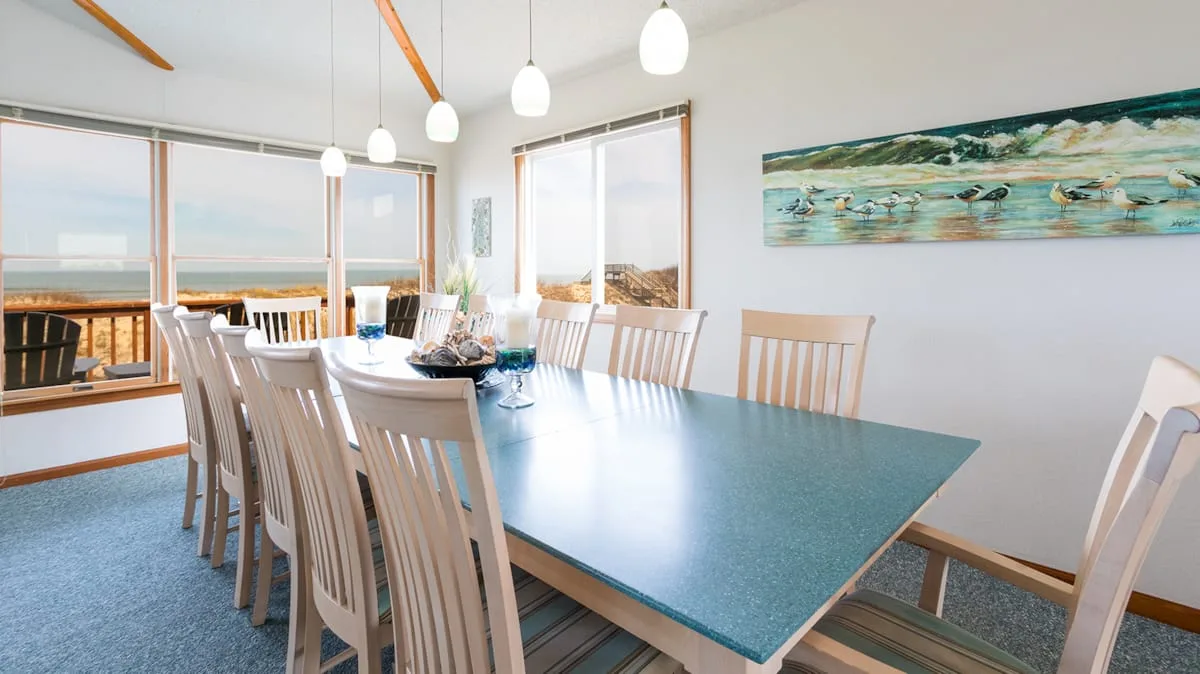 Un comedor luminoso con una mesa larga y sillas junto a grandes ventanas.