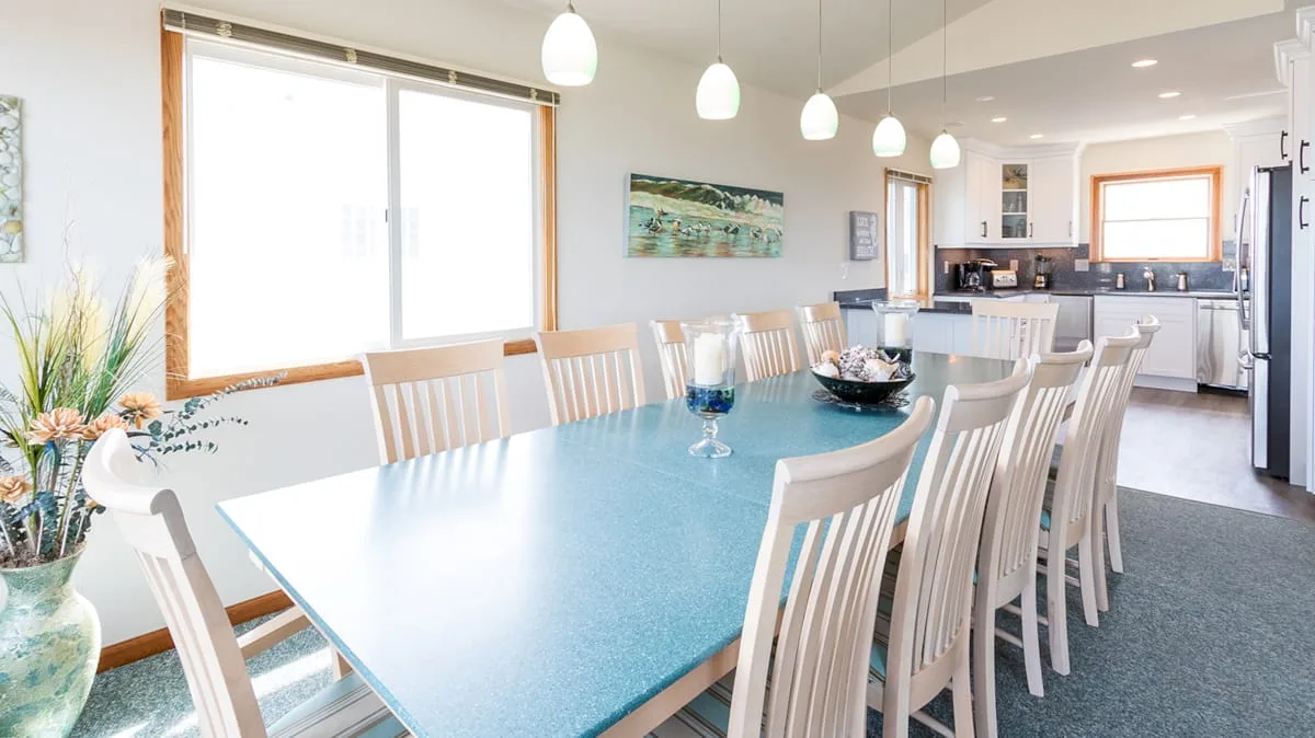 Un comedor luminoso con una mesa larga y la cocina al fondo.