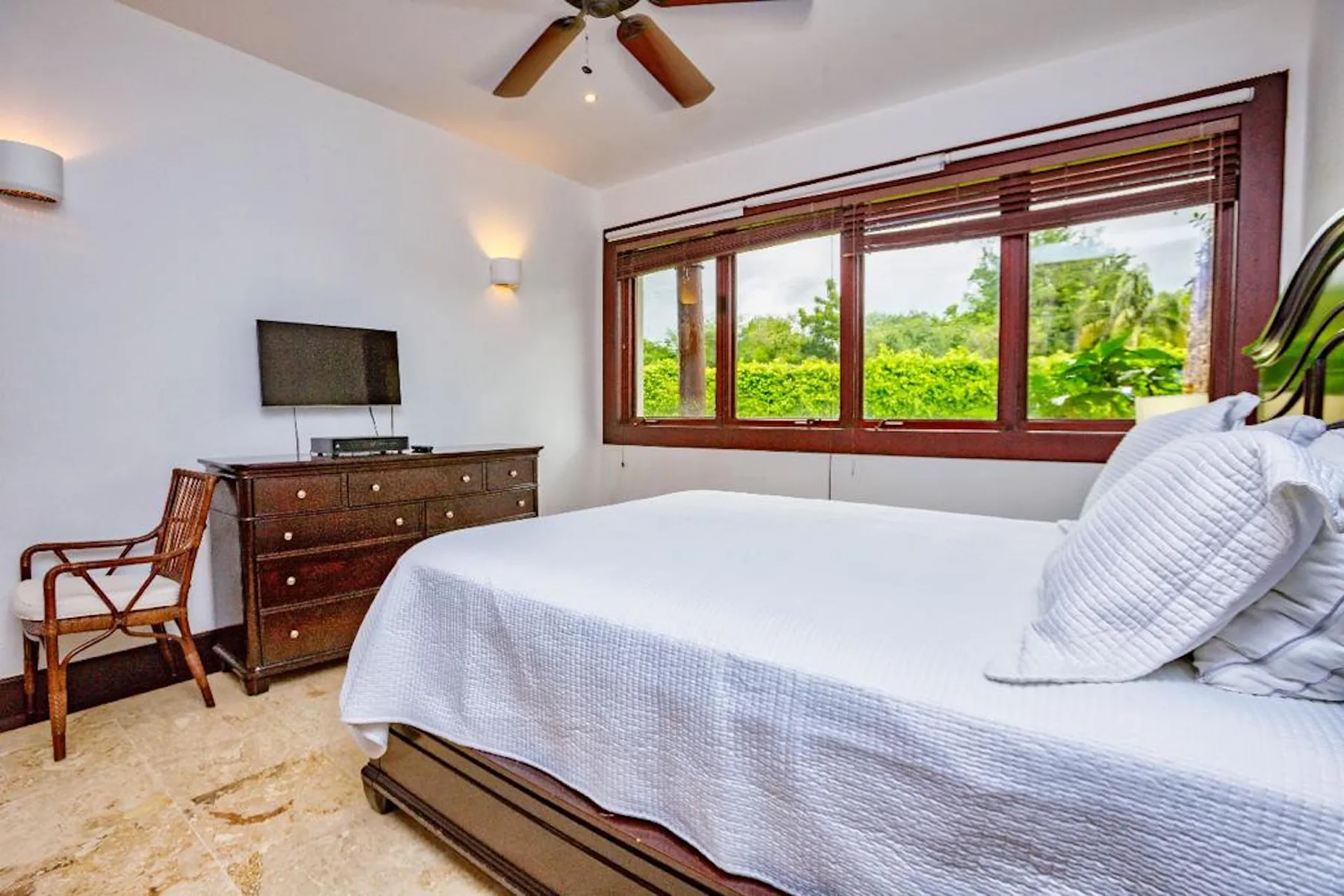 Dormitorio con una cama bien tendida junto a una amplia ventana con vistas a la vegetación.